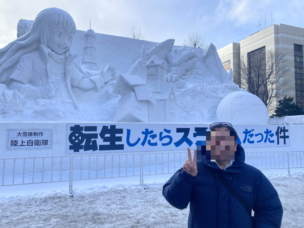 札幌雪祭りの巨大な転生したらスライムだった件の雪像前で記念撮影する筆者。好きな作品に背中を押されて旅を続ける人生を綴った記事。
