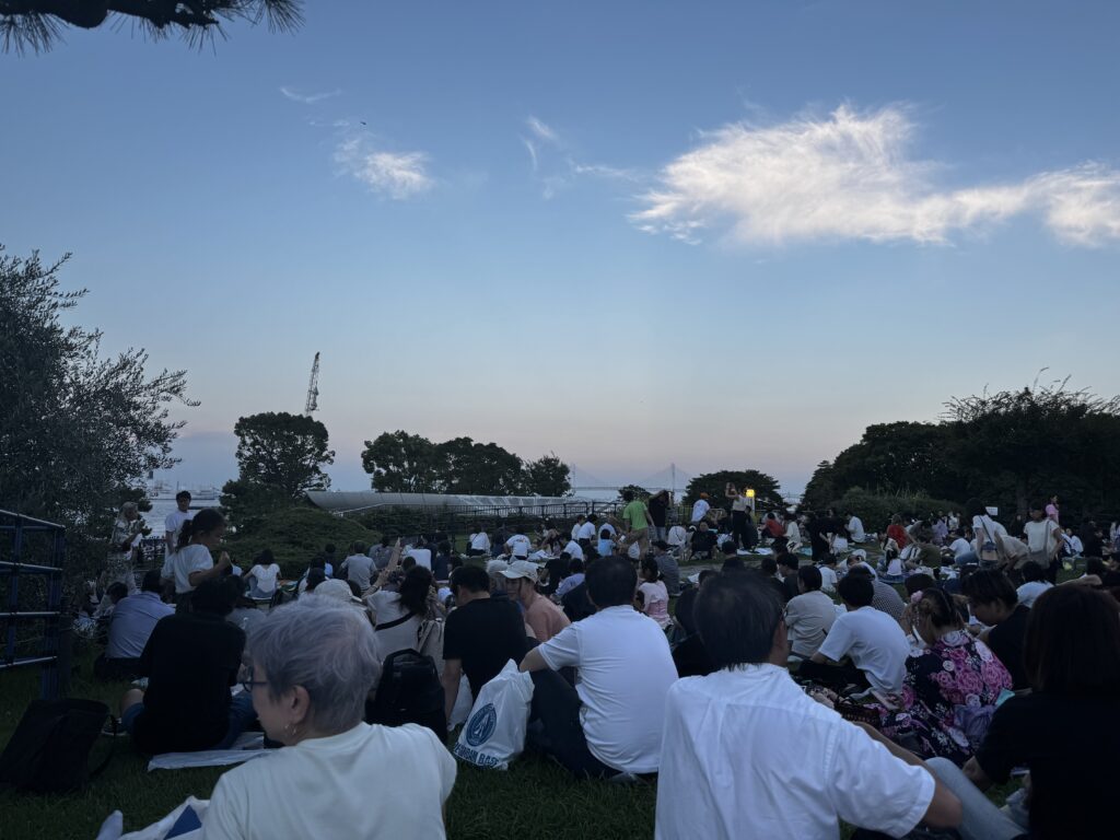 みなとみらいの花火大会を待つ臨港パークの芝生席。海を望む会場に多くの観客が集まっている。